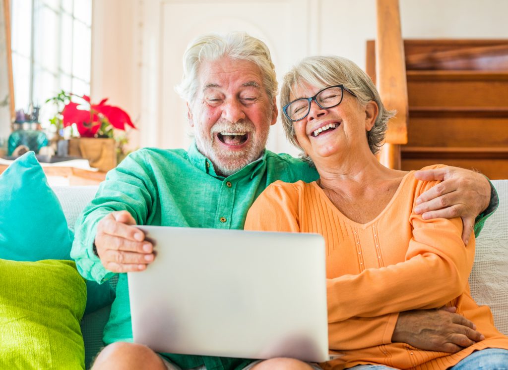 A retired couple relaxing and laughing watching a laptop in their living room