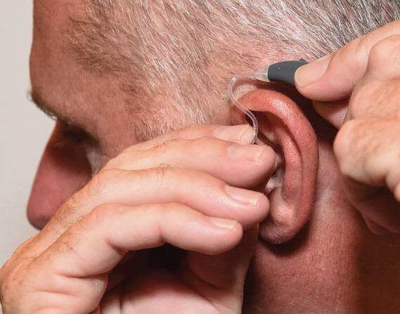 A man placing a hearing device over his ear
